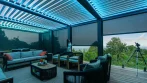 Intérieur d’une pergola de terrasse avec écrans d’intimité baissés, lames éclairées en DEL bleu et coin salon