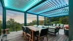 Terrasse et pergola aux lames blanches éclairées en DEL turquoise au-dessus d’un coin repas extérieur