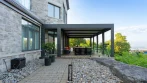 Vue de côté d’une pergola en aluminium pour terrasse, prise depuis l’allée en pierre du patio