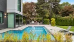 Low drone view across the pool to the covered outdoor kitchen, with the dining pergola attached to the modern house on the left