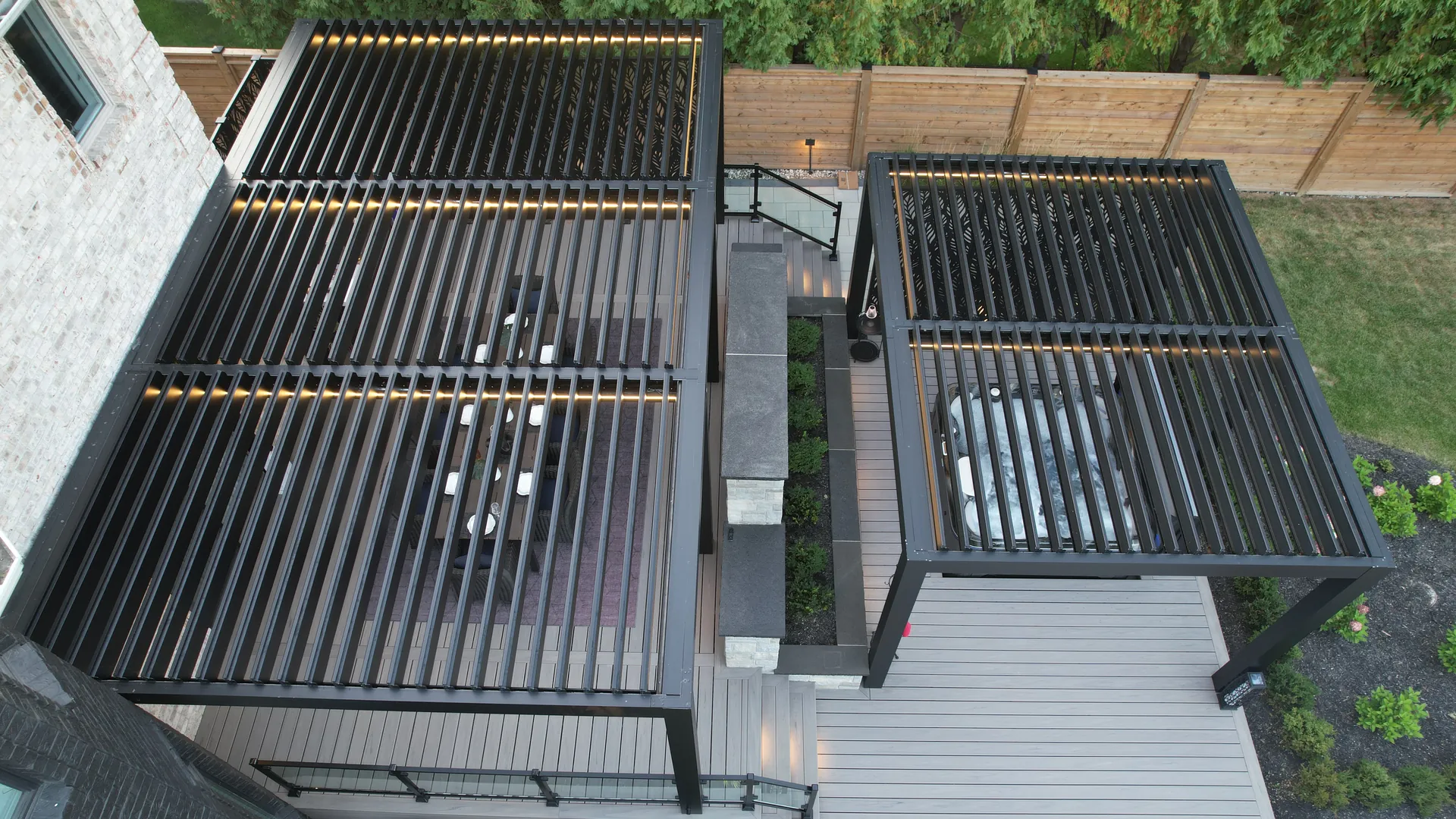 Top view of two black louvered pergolas with open louvers: a 27' x 17' dining pergola and a 17' x 14' pergola over the hot tub