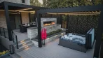 Backyard Pergola - photo 1 Black aluminum backyard pergola over a hot tub at dusk, with a stone fireplace and a second pergola over the dining area behind it