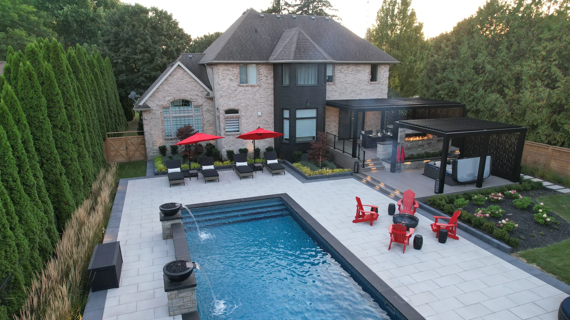 Backyard with a pool, landscaping and two black aluminum pergolas on the deck behind a brick home in Chatham, Ontario