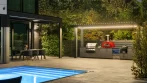 Covered outdoor kitchen at night with LED-lit louvers, next to the dining pergola and the lit pool