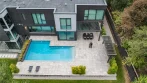 Aerial view of a modern home with a pool, a dining pergola attached to the house and a freestanding outdoor kitchen pergola along the fence