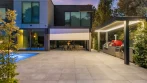 Patio at dusk with the lit outdoor kitchen pergola on the right and a white motorized zip screen half lowered on the house pergola