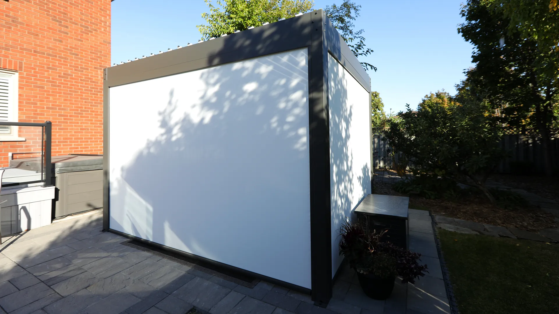 Grey aluminum pergola with white ZIP screens fully lowered on two sides for privacy beside a backyard hot tub