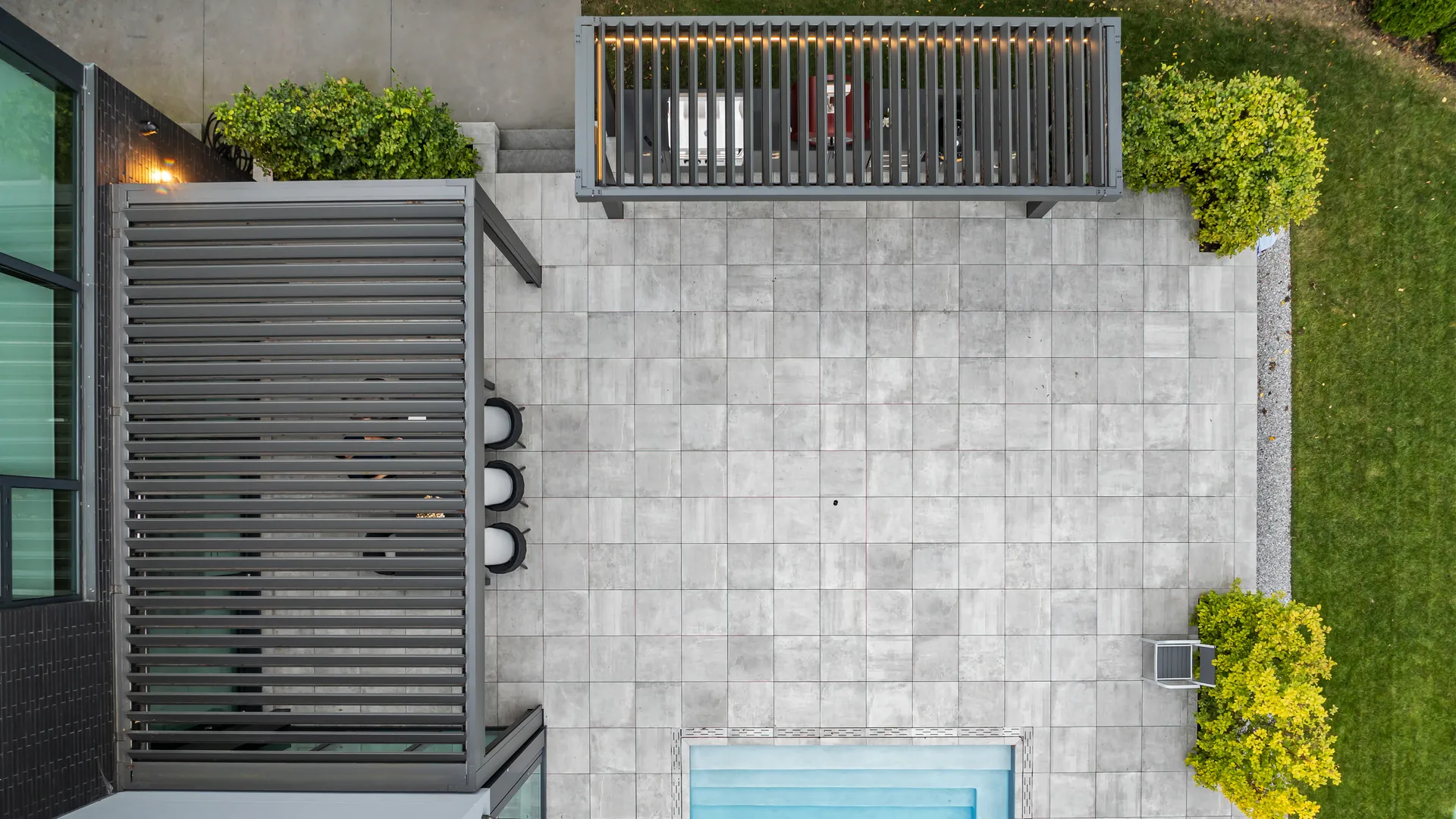Top view of two louvered roofs: the outdoor kitchen pergola at the top of the patio and the dining pergola beside the house