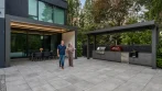Two aluminum pergolas on a patio: one attached to the house over the dining table and a freestanding pergola over the outdoor kitchen