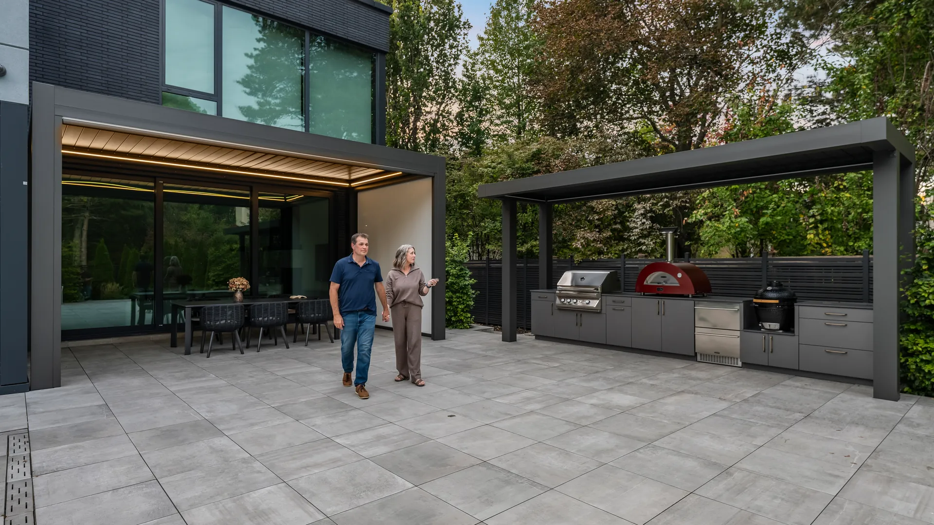 Two aluminum pergolas on a patio: one attached to the house over the dining table and a freestanding pergola over the outdoor kitchen