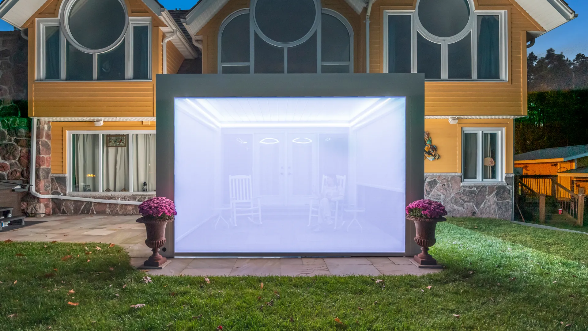 White pergola ZIP screen lit from inside at night, with rocking chairs and a seated person visible as silhouettes