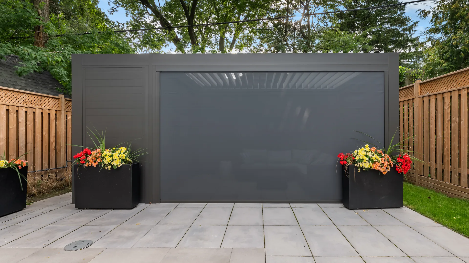 Grey aluminum pergola with a lowered ZIP screen held in side tracks below the top cassette, next to a privacy wall panel
