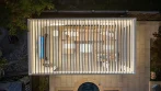 Top view of a pool pergola at night with open louvers and LED lighting over a sectional sofa and TV