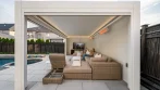 Side view of a poolside pergola lounge with a TV, heaters and LED lights, the pool and spa right beside it