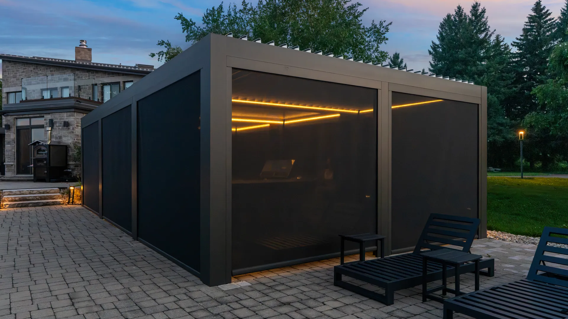 Aluminum louvered pergola with retractable ZIP screens lowered on every side and warm LED lighting at dusk